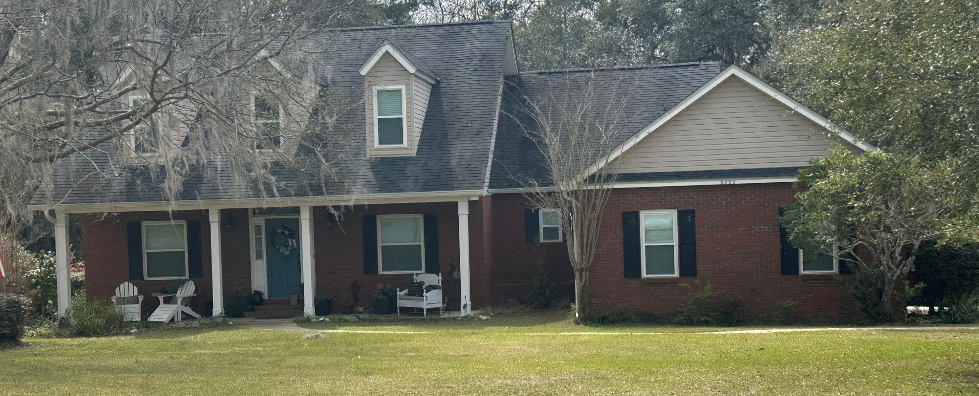 Red brick cape cod with white windows and taupe siding