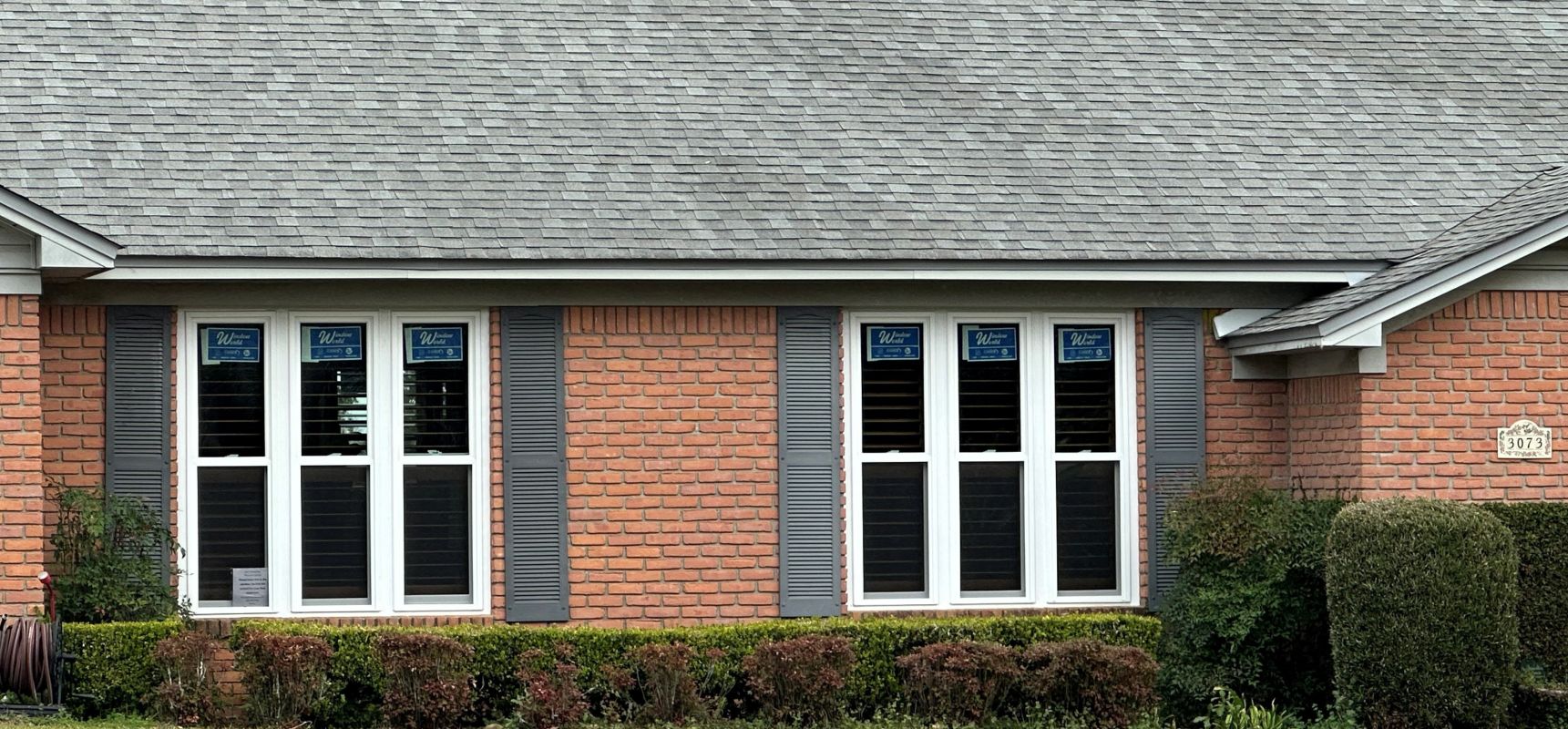 White triple windows with red brick and grey shutters